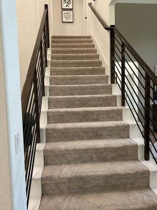 A carpeted staircase with sleek dark railings and framed art, leading to the upper floor.