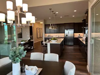 A modern kitchen and dining room with dark wood cabinetry, sleek appliances, and elegant lighting.