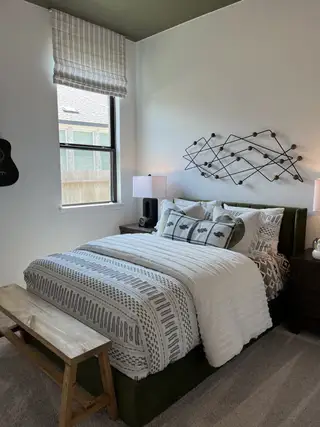 A cozy bedroom featuring patterned bedding, wall art, and elegant lighting, complemented by a wooden bench and natural light.