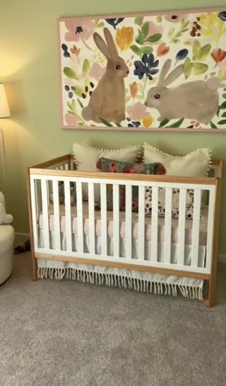 A cozy nursery with a wooden crib, plush pillows, and playful rabbit artwork on pastel walls.