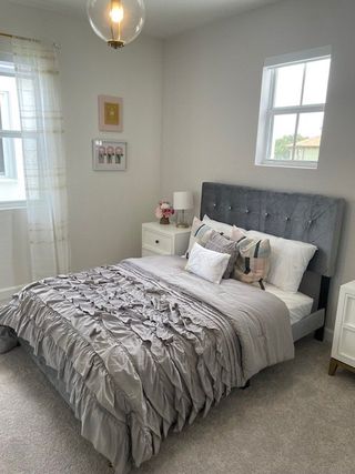 A cozy bedroom featuring a tufted bed, elegant gray bedding, light-filled windows, and chic decor accents.