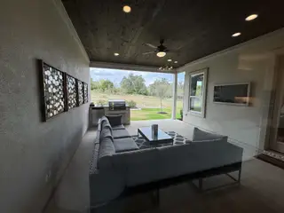 A cozy outdoor patio with a modern sofa, TV, and barbecue setup, offering scenic views of the lush landscape.