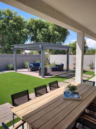 A beautiful backyard patio with a wooden dining table, pergola, and lush greenery for outdoor leisure and entertaining.