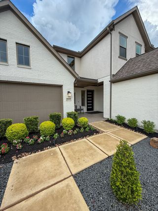 A modern white brick home with lush landscaping in Marvida by New Home Co. (Cypress, TX).