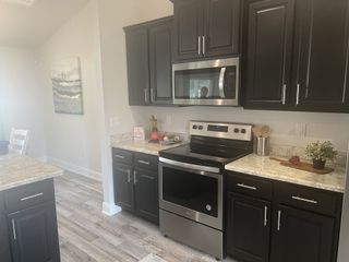 Modern kitchen featuring sleek dark cabinetry, stainless steel appliances, and a granite countertop with light wood flooring.
