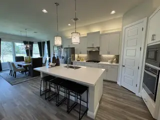 A modern kitchen with sleek white cabinetry, quartz countertops, and pendant lighting, opening to a spacious dining area.