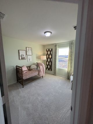 Model Home A cozy nursery with a soft green wall, art, a crib, and natural light from a large window with patterned curtains.