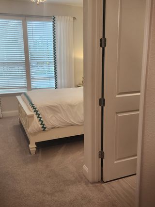 A cozy bedroom with plush carpet, elegant white drapery, and a neatly dressed bed exuding warmth and comfort.