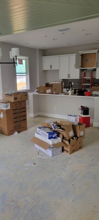 A modern kitchen under construction with white cabinets, boxed appliances, and stylish lighting.