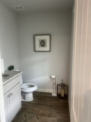 Model Home A cozy bathroom featuring wood floors, a white vanity, and minimalist decor with a subtle art piece.