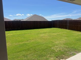 Street view A lush green backyard with a wooden fence under a clear blue sky in Frontier Pointe by D.R. Horton (Princeton, TX).