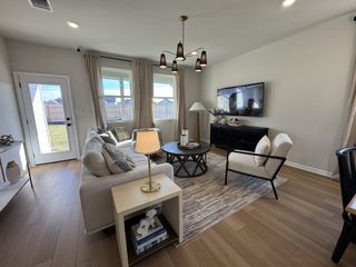 Model Home A cozy living room featuring a plush sofa, elegant chairs, and a modern TV setup, illuminated by chic lighting.