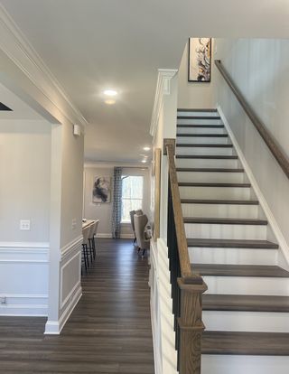 Model Home An elegant hallway with wooden flooring, crown molding, and a modern staircase leading upstairs.