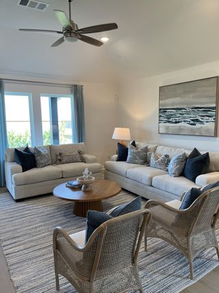 A cozy living room features plush sofas, wicker chairs, and a round wooden table, complete with soft lighting and serene artwork.