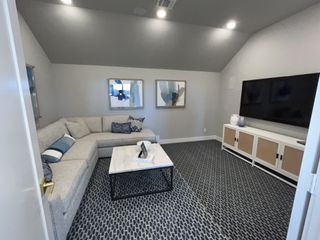 Model Home A cozy media room featuring a modern sectional sofa, a large TV, and chic decor with patterned carpeting.