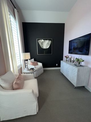 A chic relaxation space with soft pink and black walls, white armchairs, and elegant floral artwork.