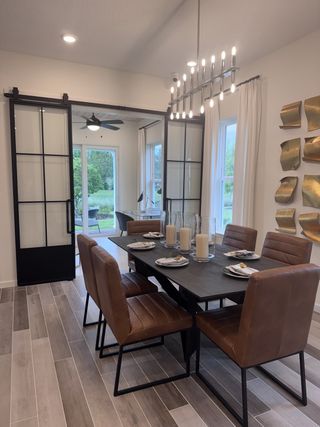 A modern dining area with sleek brown chairs, a black table, and stylish lighting, featuring glass sliding doors.