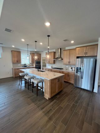 A modern kitchen with wooden cabinetry, a marble-topped island, and sleek stainless steel appliances.