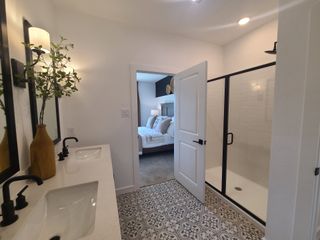 Model Home A chic bathroom featuring patterned tiles, dual sinks, a minimalist shower, and a view into a cozy bedroom.