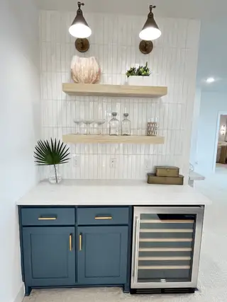 Model Home A chic beverage nook with navy cabinets, open shelves, and a wine cooler under elegant wall sconces.