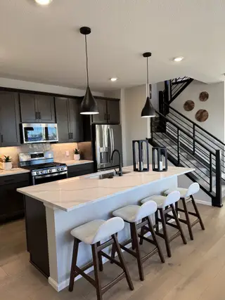 A modern kitchen with dark cabinets, sleek island seating, pendant lighting, and stainless appliances.