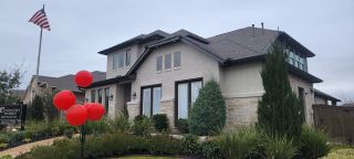 A stately two-story home with a stone and stucco facade, featuring red balloons and an American flag, in Davis Ranch by Coventry Homes (San Antonio, TX).