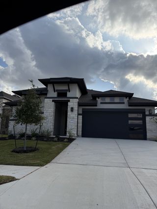 Street view A modern stone home with a sleek design and manicured lawn in Carillon by Brightland Homes (Manor, TX).