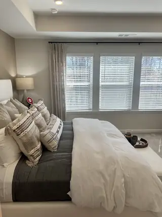 A sophisticated primary bedroom with large windows, soft layered bedding, and a tranquil neutral color palette.