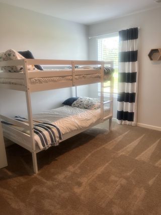 Cozy bedroom with white bunk beds, striped curtains, and soft carpeting for a welcoming atmosphere.