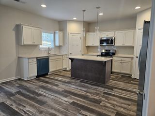 Model Home Bright kitchen with white cabinetry, stainless appliances, a center island, and dark wood flooring.