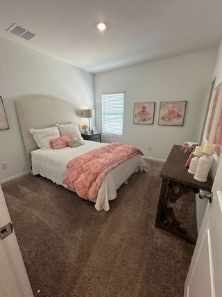 Model Home A cozy bedroom featuring a plush carpet, elegant bed with pink accents, and tasteful wall art.