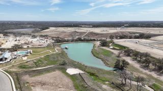 A scenic aerial view of a developing community with a pond and amenities in Lariat 60' by Coventry Homes, Liberty Hill, TX.