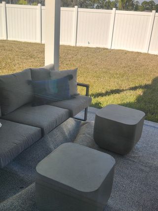 A cozy outdoor patio with a sleek gray sofa, plush cushions, and modern cube tables on a textured rug.