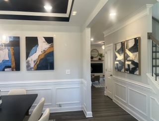 Model Home A modern hallway featuring abstract art, elegant wainscoting, and recessed lighting, leading to a cozy living area.