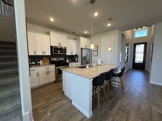 A modern kitchen with white cabinets, granite island, pendant lighting, and stainless appliances.