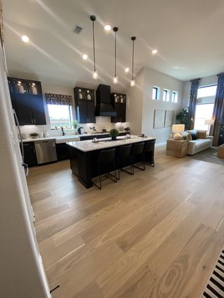 Model Home Modern kitchen with dark cabinets, island seating, and elegant pendant lights, opening to a cozy living area with natural light.