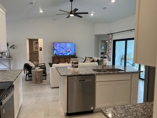A modern open-concept living area with granite countertops, cozy seating, and a large TV, featuring sliding glass doors.