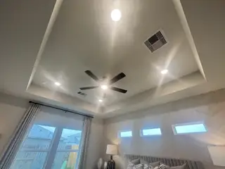 A modern bedroom ceiling with recessed lighting, tray ceiling, ceiling fan, and large window for natural light.