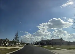 A peaceful street view in Cross Creek by D.R. Horton (Green Cove Springs, FL) features paved roads, single-story homes, and a bright, sunny sky.
