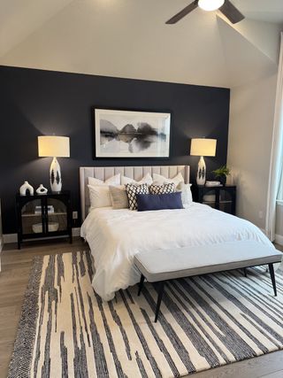 A modern bedroom featuring a navy accent wall, cozy bedding, stylish lamps, and a patterned rug.