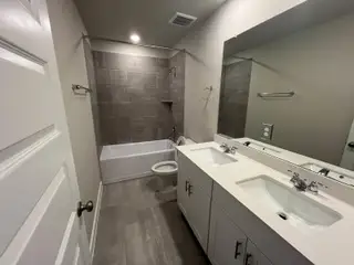 A modern bathroom with dual sinks, sleek countertops, a tiled bathtub, and contemporary fixtures.