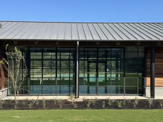 Community Amenities A modern building with glass walls and metal roofing in Parkside on the River by Coventry Homes (Georgetown, TX).