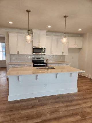 A sleek kitchen with white cabinets, a central island, pendant lighting, and stainless steel appliances.