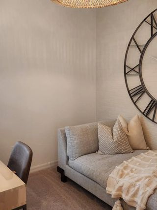 Model Home A cozy room with a soft gray sofa, textured pillows, a woven light fixture, and a large wall clock for a chic touch.