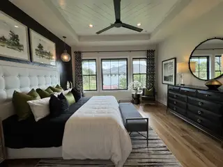 Model Home A sophisticated bedroom with a tufted headboard, elegant decor, and abundant natural light from large windows.