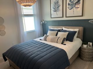 A cozy bedroom with a navy quilt, woven pendant light, and botanical art creates a serene, inviting atmosphere.