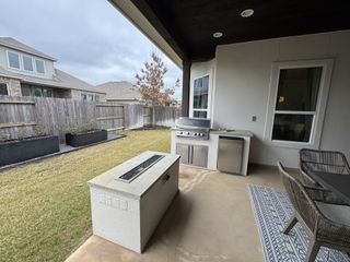 A covered outdoor dining space with a built-in TV, ceiling fan, and grill station in Veramendi by Scott Felder Homes (New Braunfels, TX).