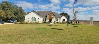 Charming white stone home with lush yard in Pradera Ridge by Texas Homes (Floresville, TX).