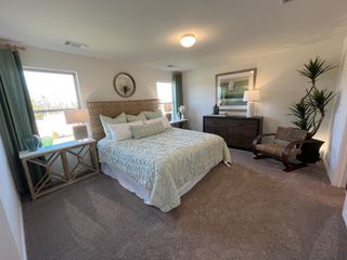 A serene primary bedroom with a woven headboard, soft carpeting, and large windows bringing in natural light for a cozy retreat.
