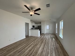 Model Home An airy living area with wood floors, a ceiling fan, and a modern open kitchen boasting sleek white cabinetry.